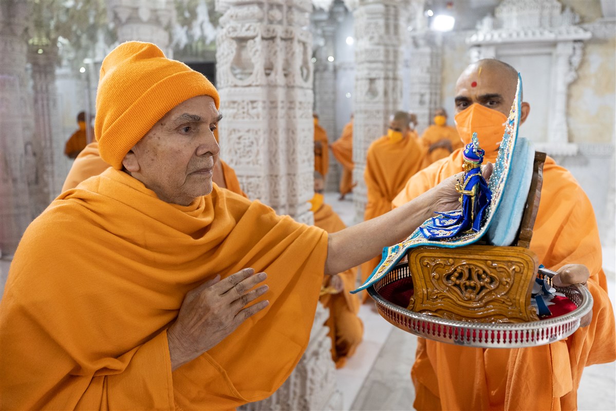 Swamishri meticulously adjusts the attire of Shri Akshar Purushottam Maharaj