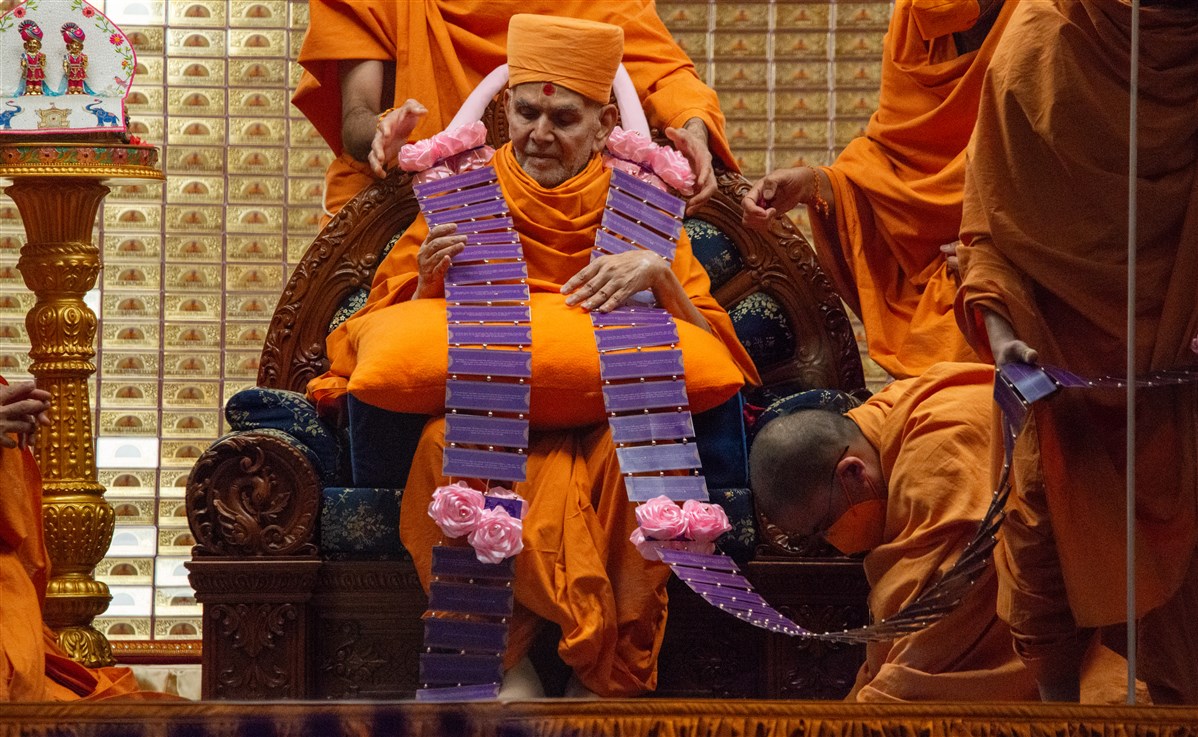 Swamis honour Swamishri with a long garland..