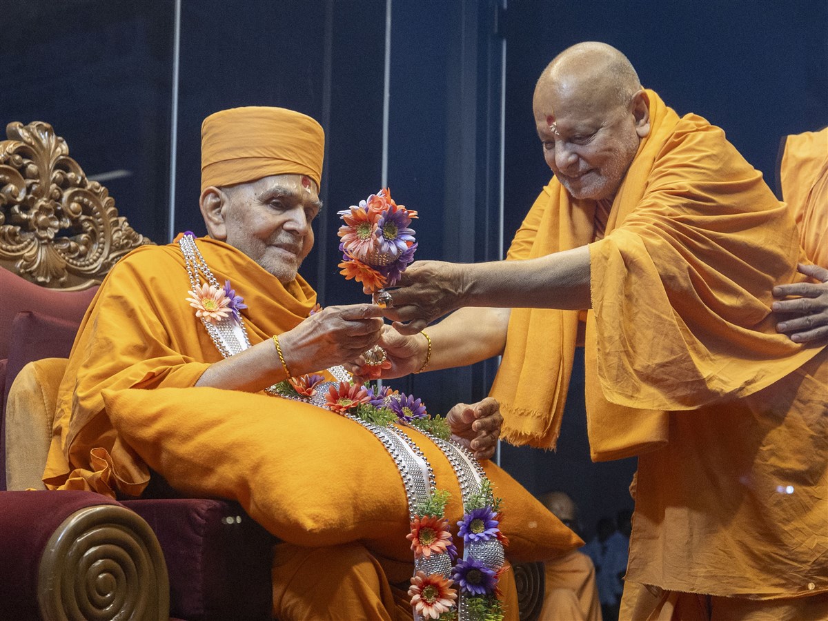Sadguru Ishwarcharandas Swami presents Swamishri with a garland and chhadi