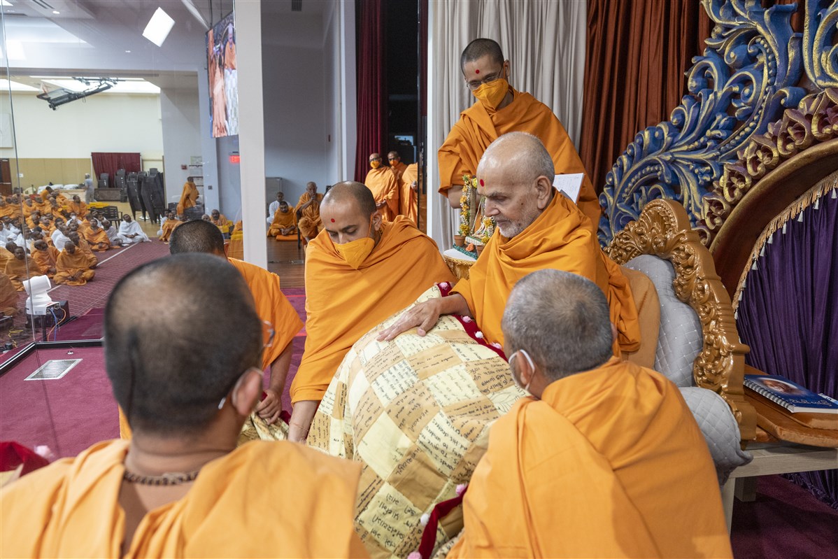 Swamis present a shawl to Swamishri bearing the prayers written by devotees