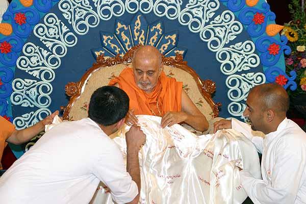 Swamishri closely looks at a shawl presented to him embroidered with the 64 characteristics of a true saint 