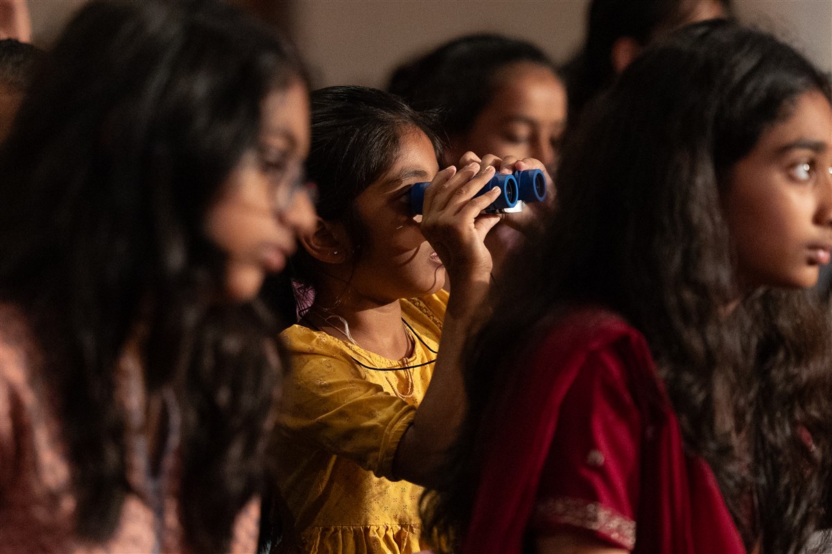 A young girl experiences the darshan of Swamishri through binoculars