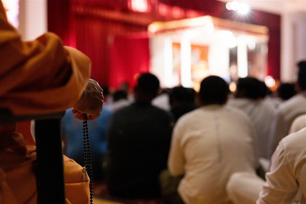 A swami turning the rosary during Swamishri's puja