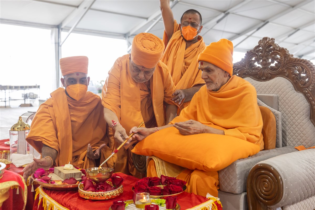 Swamishri takes flame from the lamp ignited on <a href="https://www.baps.org/Vicharan/2023/25-June-2023-23741.aspx" target="blank" style="text-decoration:underline; color:blue;">June 25, 2023</a>  for the Agni Sthapan Vidhi