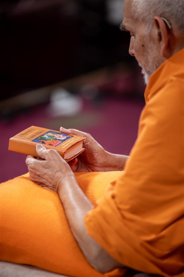 Swamishri immersed in darshan of the murtis on the top cover of Shikshapatri and Satsang Diksha