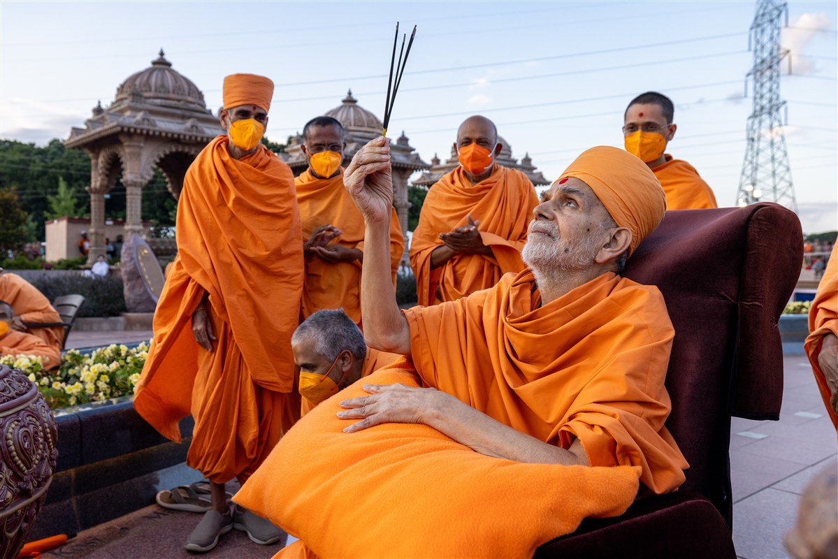Swamishri lifts incense sticks in prayer towards the magnificent 49-foot murti of Shri Nilkanth Varni