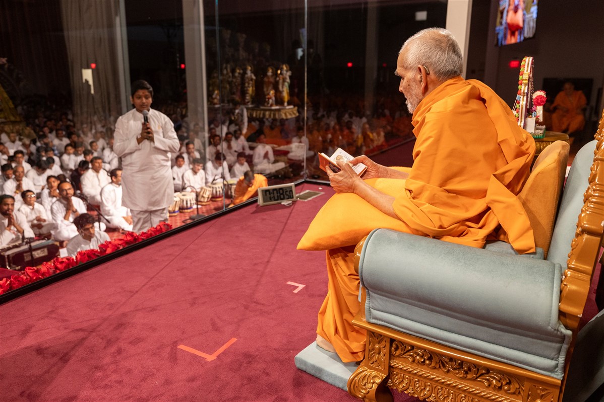 A youth leads everyone in reciting the sadhana mantra and daily prayer in Swamishri's puja 