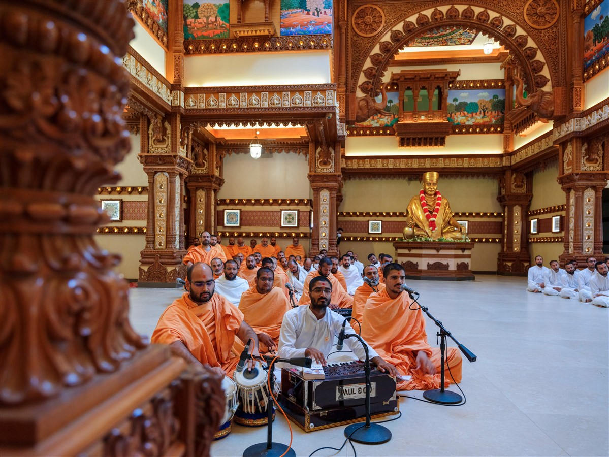 Swamis and a sadhak offer kirtan bhakti during Swamishri’s puja