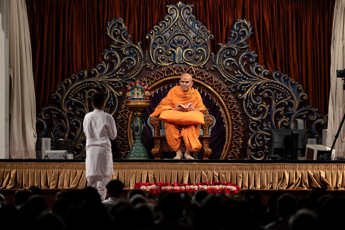 Swamishri glances at a child presenting in Swamishri's puja