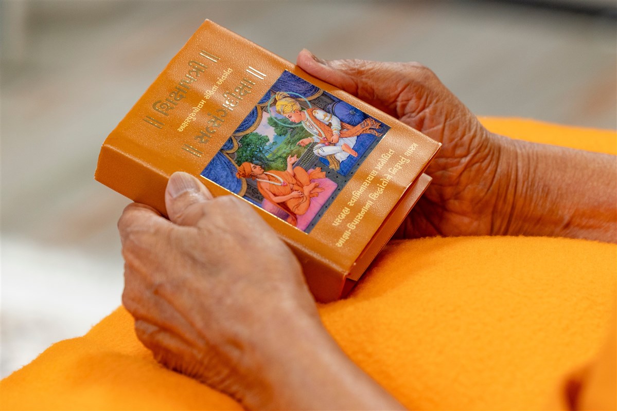 Swamishri closely observes the murti on the cover of the Shikshapatri and Satsang Diksha