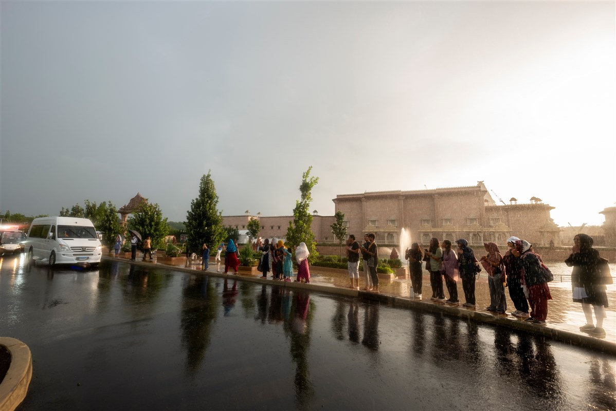 Despite the rain, devotees stand to have darshan of Swamishri