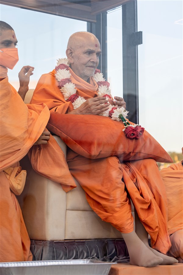 Swamishri wearing a garland listens to the presentation