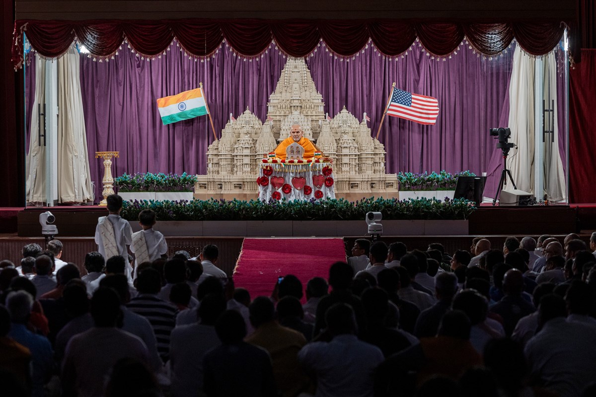 Swamishri's puja with the backdrop of the Akshardham with the Indian and American flags