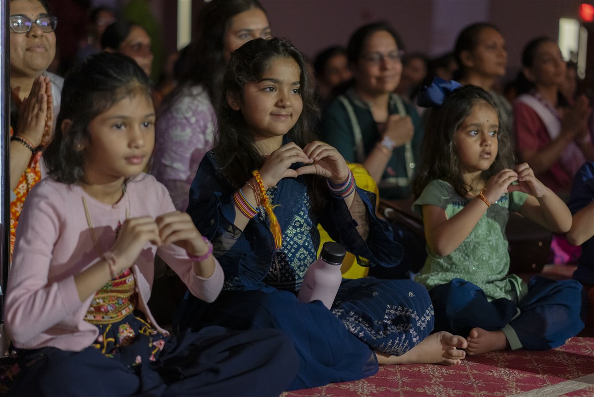 Children form hearts with their hands during the darshan of Swamishri