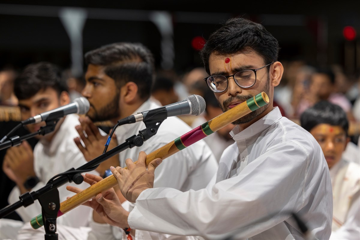 A youth plays the flute during Swamishri's puja
