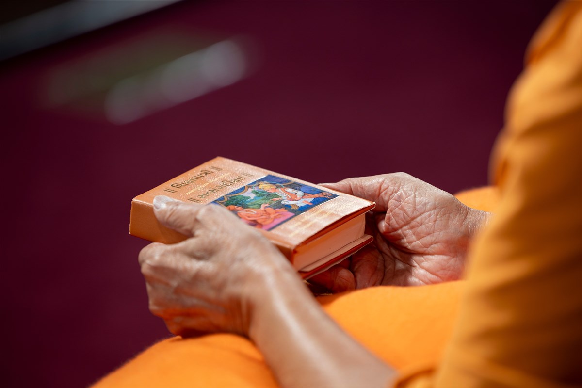 Swamishri closely observes the murti on the cover of the Shikshapatri and Satsang Diksha