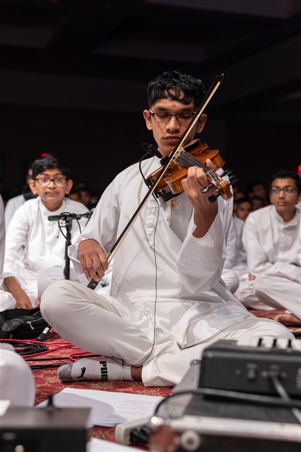 A kishore plays the violin in Swamishri's puja