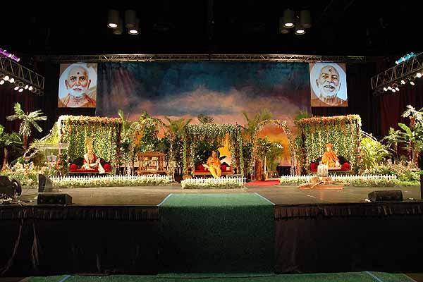 Evening ,Swamishri seated on stage amidst a garden-like setting 	