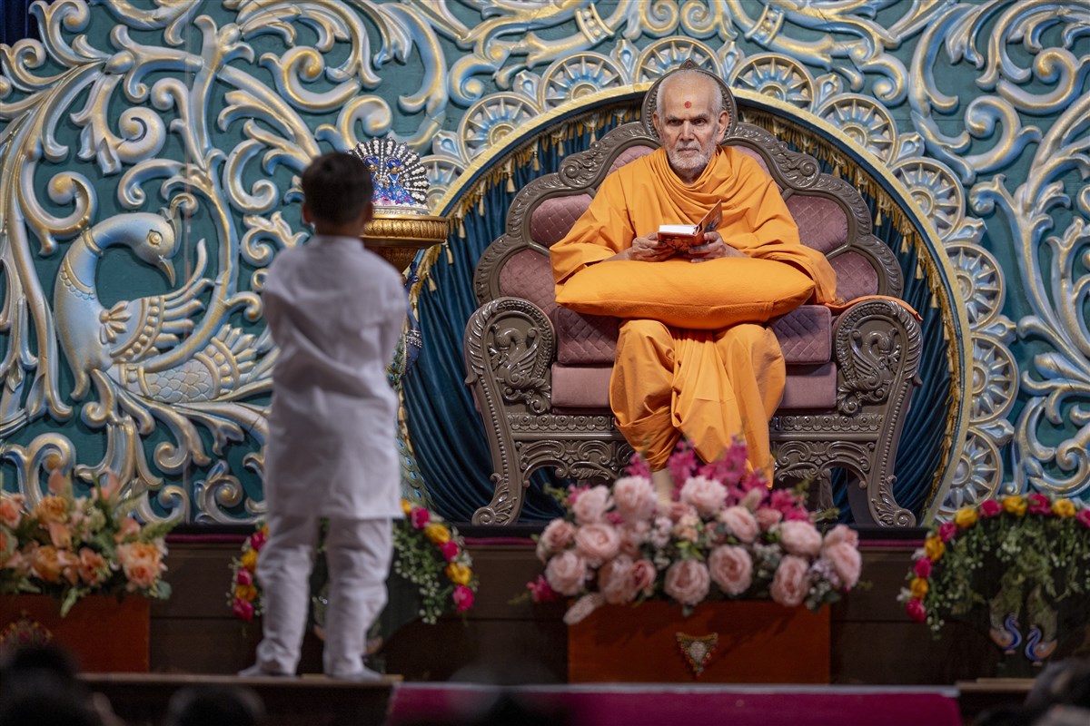 A child leads everyone in reciting the sadhana mantra and daily prayer in Swamishri's puja