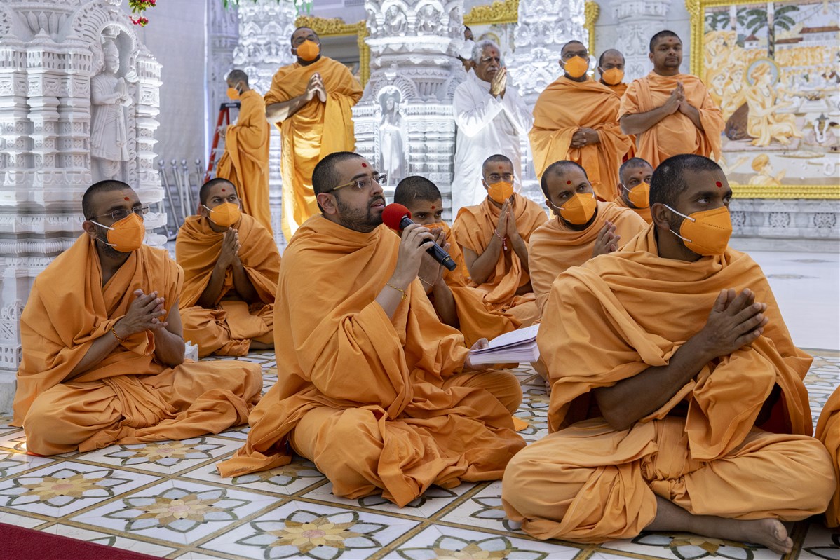 A swami sings a kirtan while Swamishri is engrossed in darshan