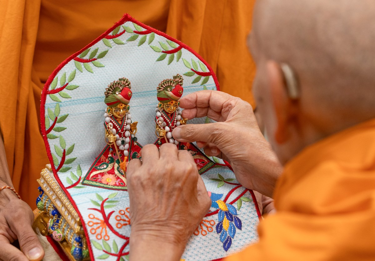 Swamishri meticulously adjusts the attire of Shri Gunatitanand Swami Maharaj