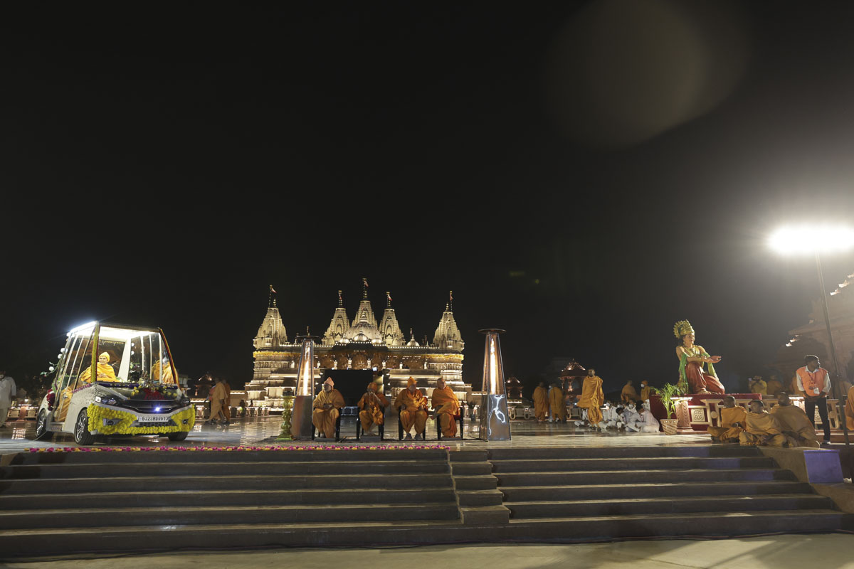 Swamishri and senior swamis observe the nagar yatra from the mandir podium