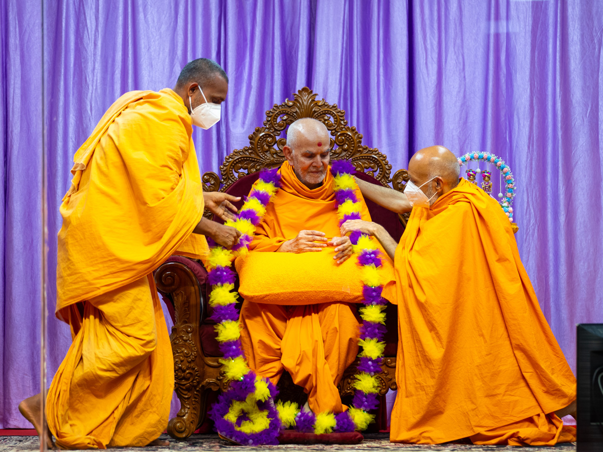 Sarvamangal Swami and a swami honor Swamishri with a garland