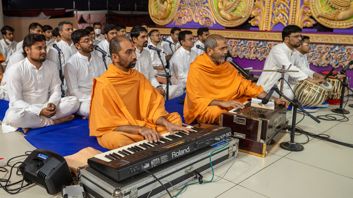 A swami and youths sing kirtans in Swamishri's puja