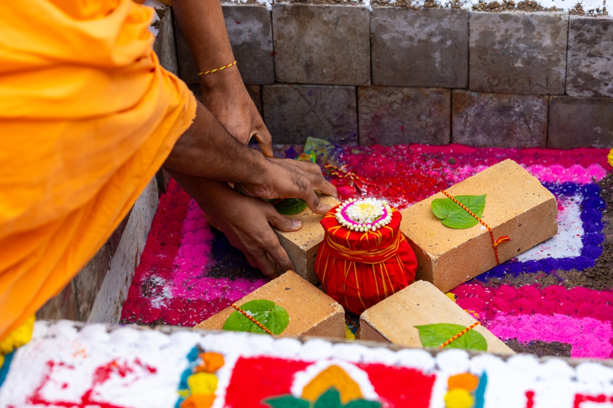 A swami and a devotee place a sanctified brick