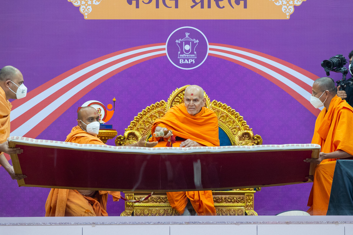Swamishri sprays sanctified saffron-scented water on the names of karyakars