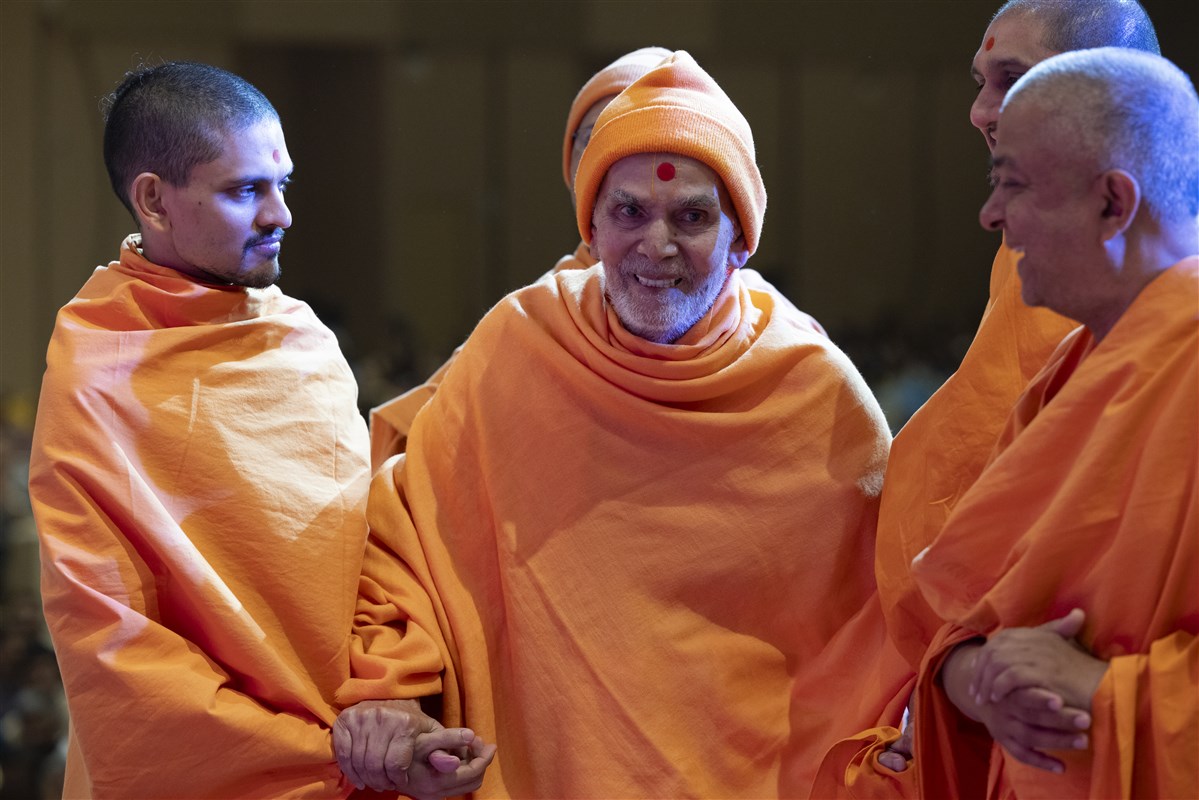 Swamishri shares a light moment with swamis as he departs the assembly hall