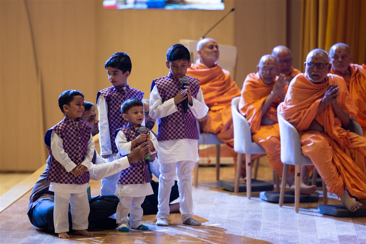 A young child leads everyone in reciting the sadhana mantra and daily prayer in Swamishri's puja