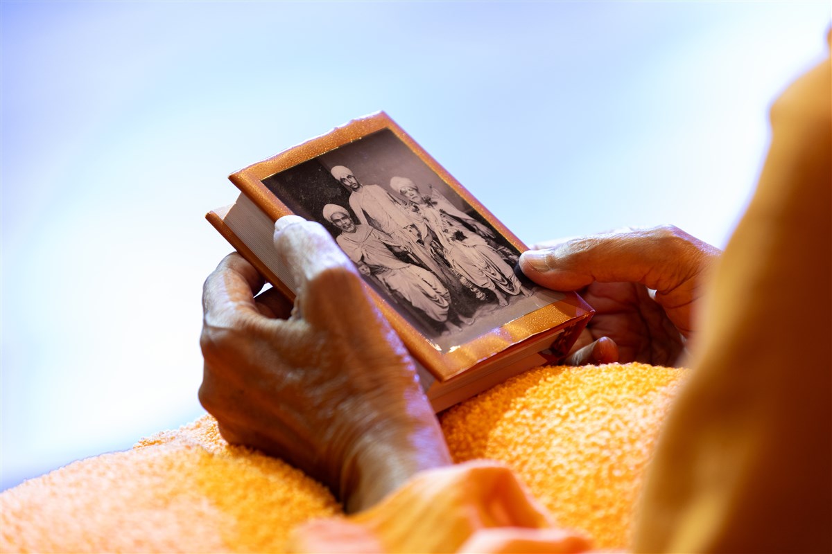 Swamishri doing darshan of Shastriji Maharaj, Yogiji Maharaj and Pramukh Swami Maharaj's photo on the back  cover of the Shikshapatri and Satsang Diksha