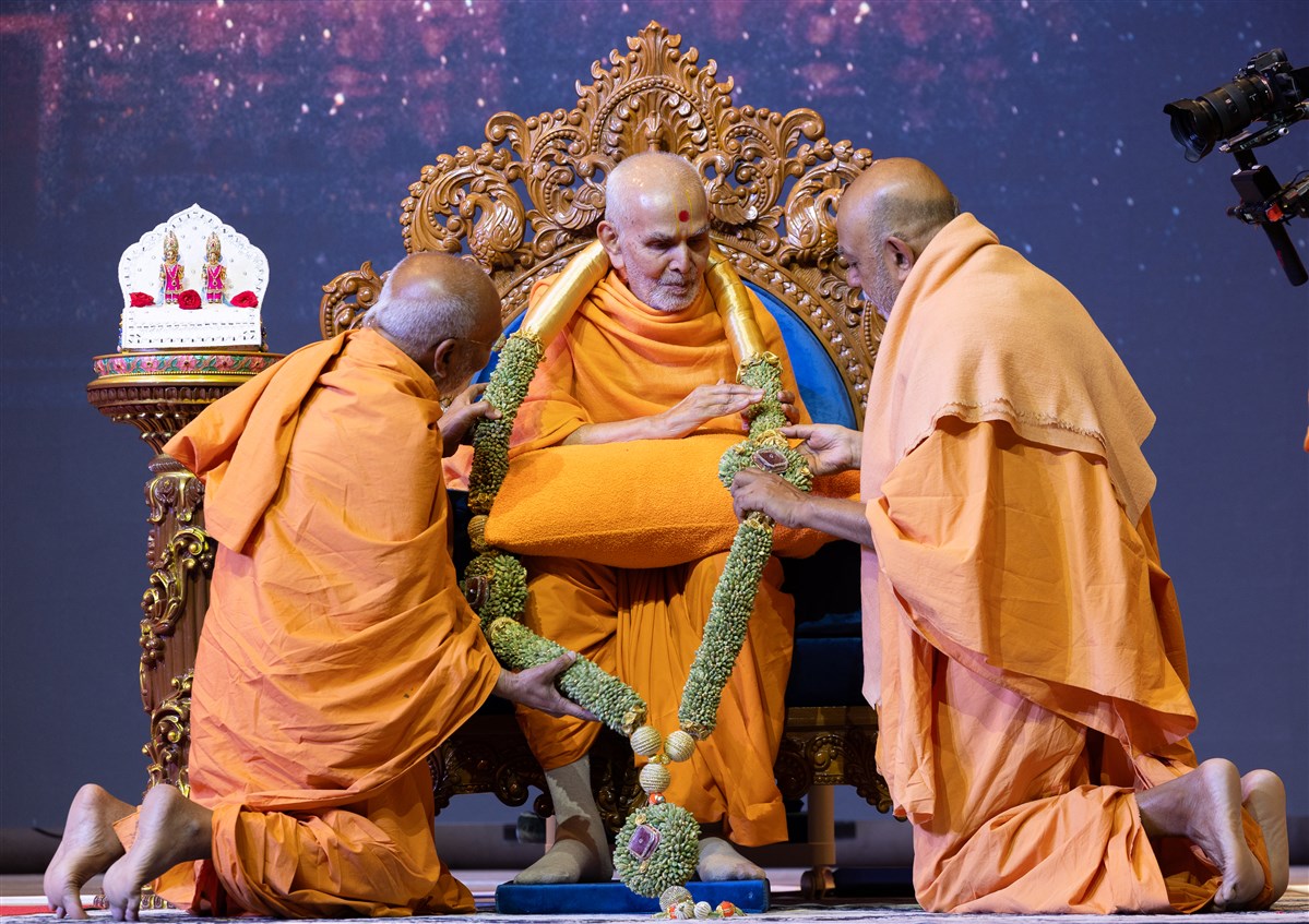 Swamis honour Swamishri with a decorative garland made of cardamom seeds