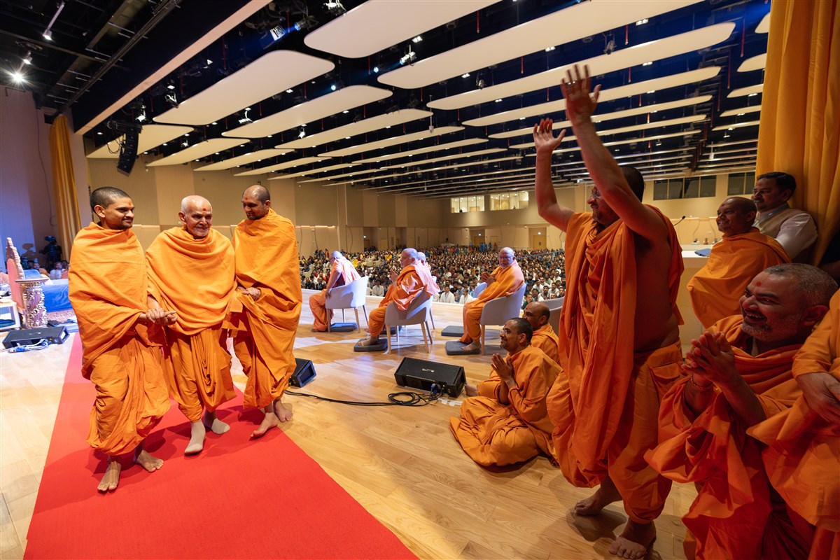 Swamishri shares a light moment with swamis as he departs the assembly hall