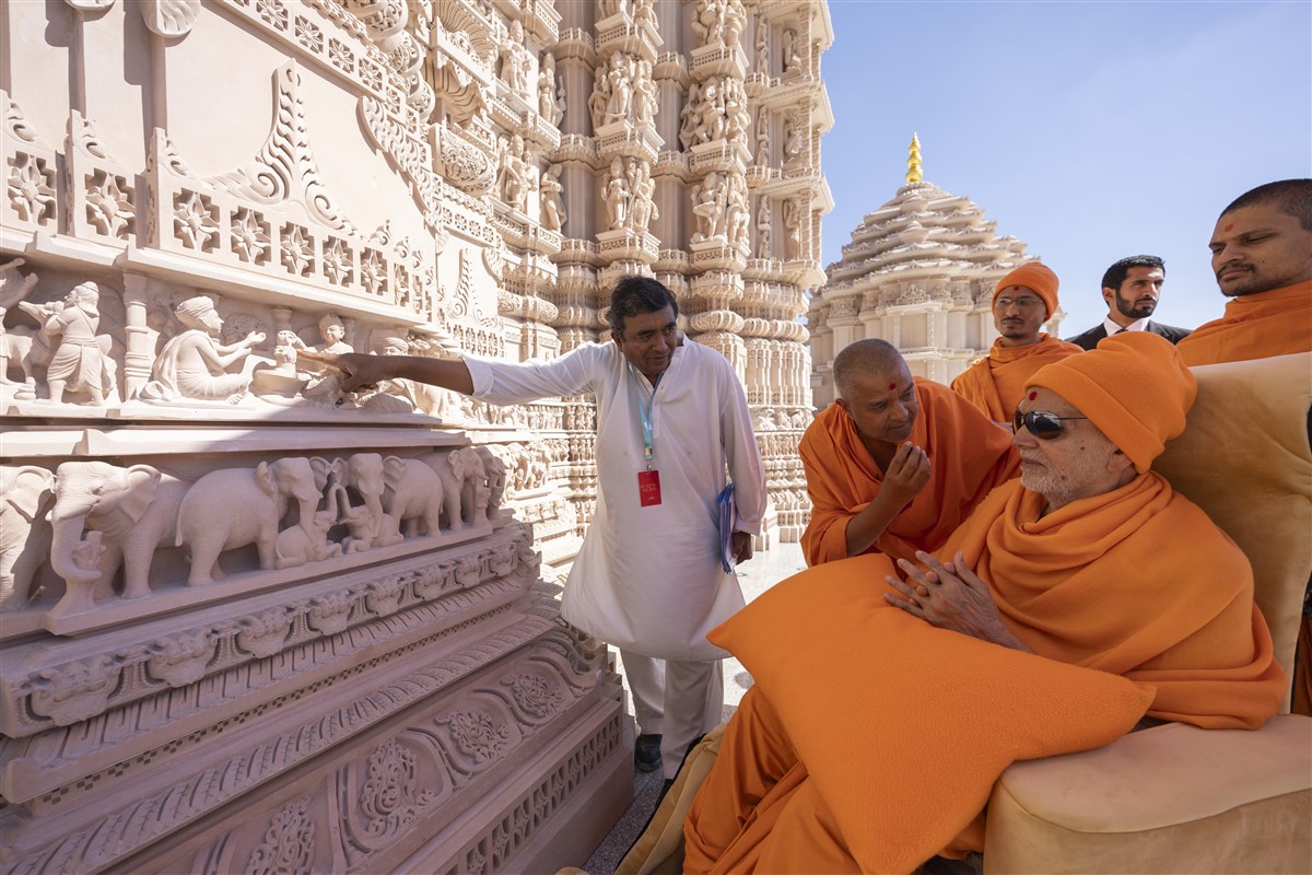 Swamishri listens attentively as a construction volunteer explains features of the mandir's exterior