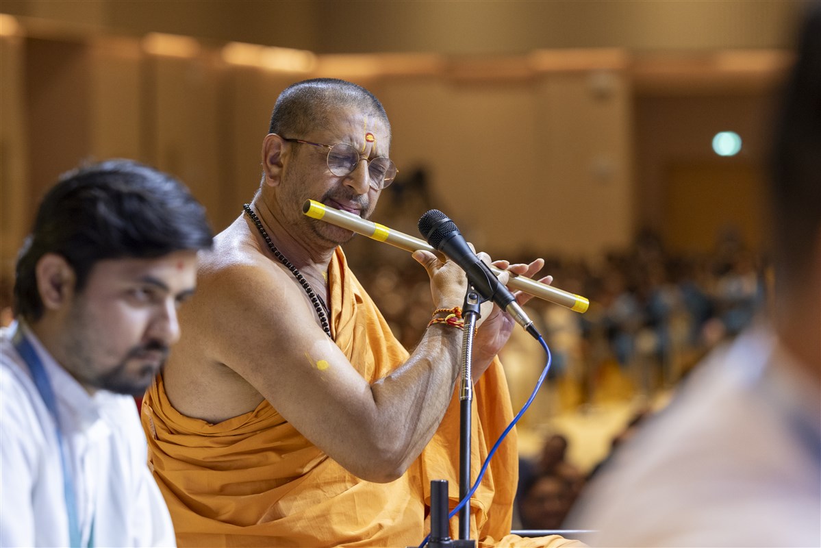 A swami plays the bansuri as Swamishri greets the devotees