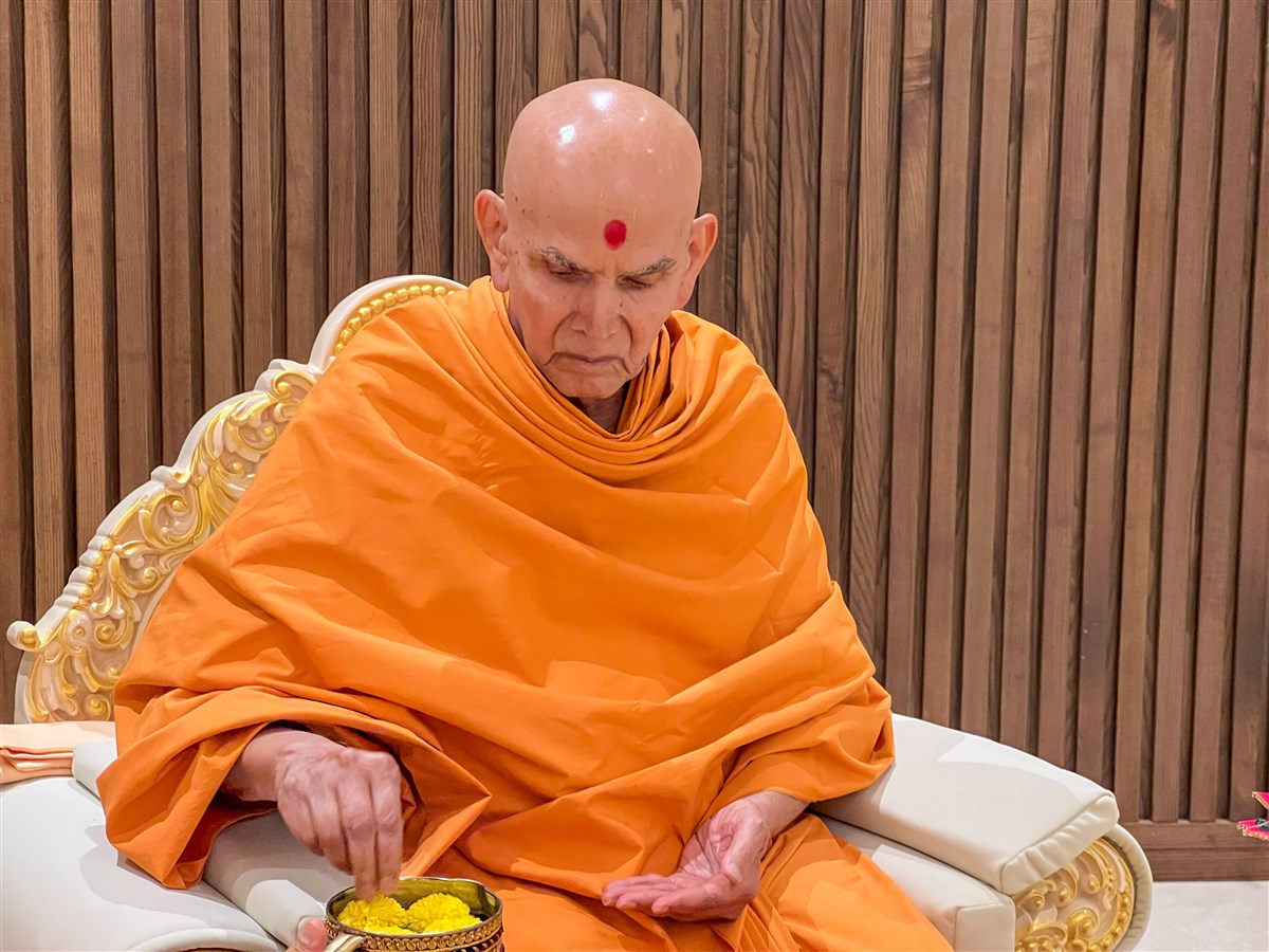 Swamishri adds flowers to the water sanctified by the holy relics of Bhagwan Swaminarayan and the Guru Parampara