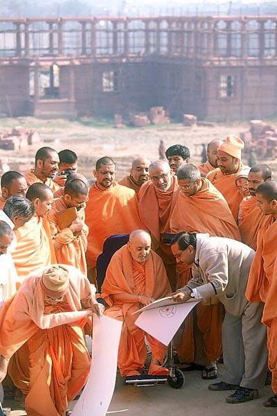  Swamishri observes the plans and discusses about the complex. In the background are sections of the parikrama