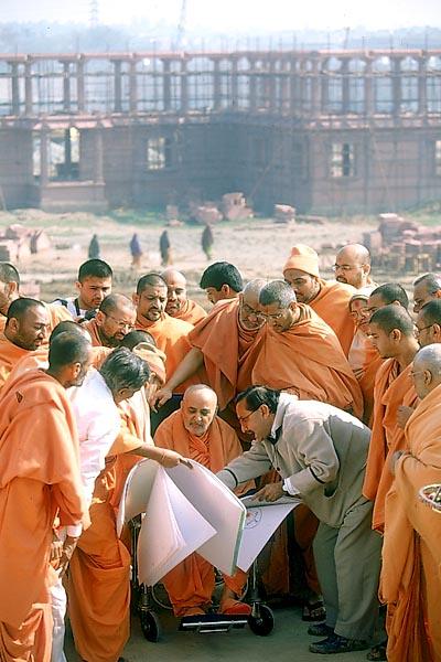  Swamishri observes the plans and discusses about the complex. In the background are sections of the parikrama