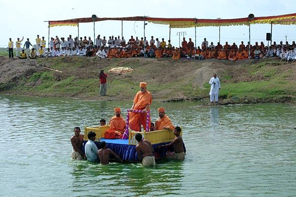 Swamishri is transported on a raft to the festival stage 	