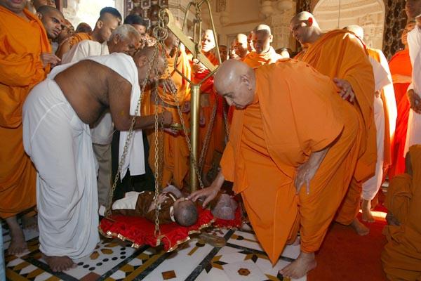 Swamishri applies chandlo to a balak during a sugar-weighing ritual (sakar tula) 	