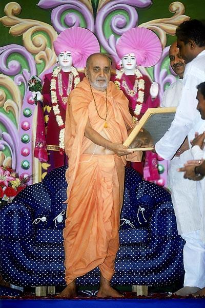 An official of the Municipality of Surendranagar presents a citation of honor to Swamishri