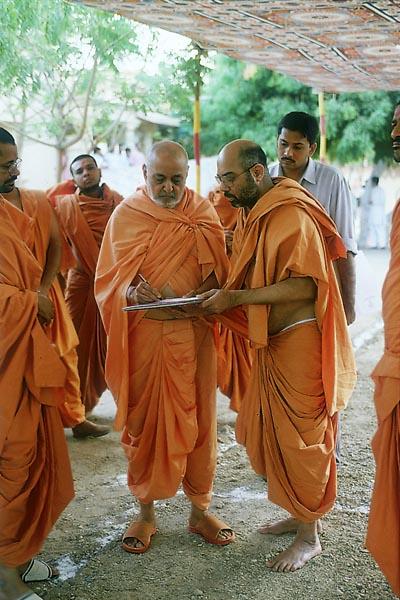 Swamishri writes a letter while standing along the way