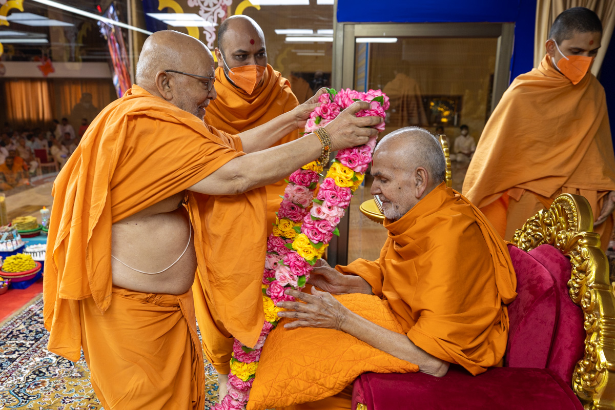 Pujya Ghanshyamcharan Swami honors Swamishri with a garland