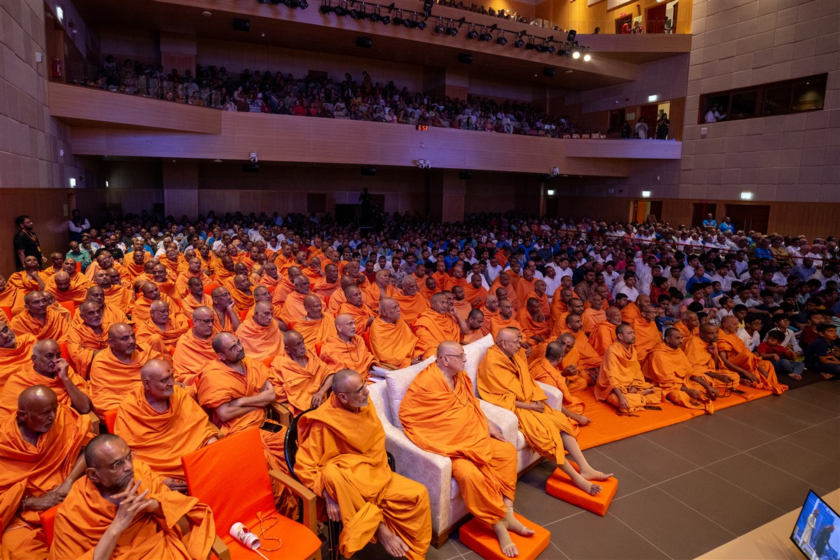 Senior swamis, swamis and devotees watch a skit performance by devotees