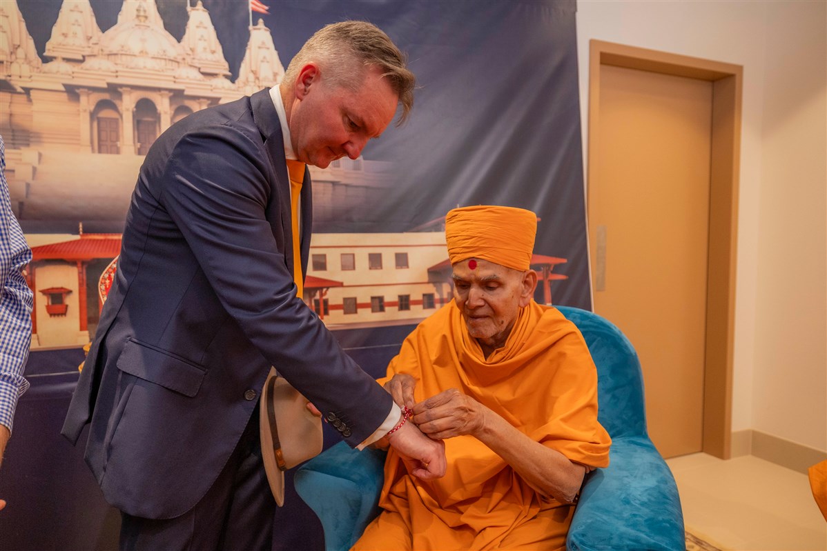 Mahant Swami Maharaj ties a Nadachadi on the wrist of Hon Chris Bowen, Minister for Climate Change and Energy of Australia 