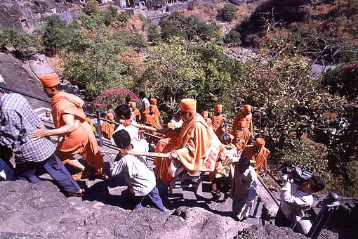 Swamishri being carried through narrow, steep pathways towards the caves
