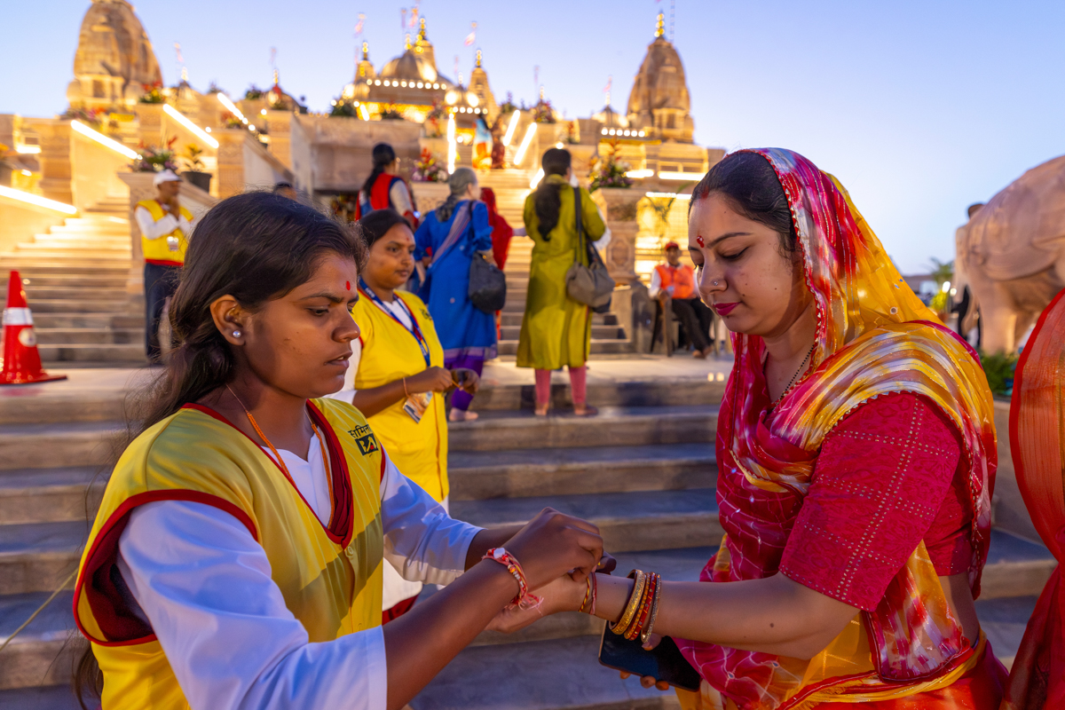 A karyakar ties a nadachhadi to a devotee as she enters for the pratishtha mahapuja