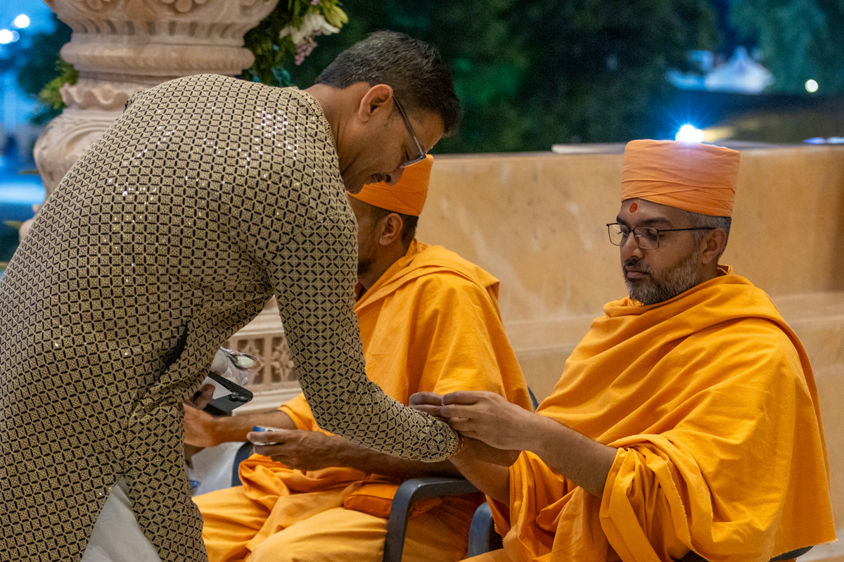 A swami ties a nadachhadi to a devotee as he enters for the pratishtha mahapuja